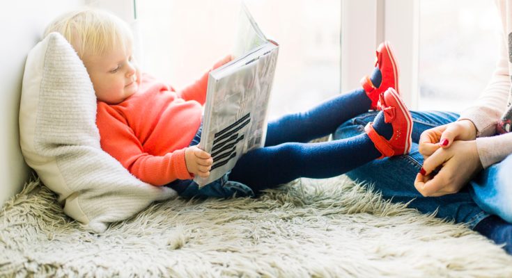 Jak być dobrym rodzicem? Dziecko czyta bajkę na łóżku.